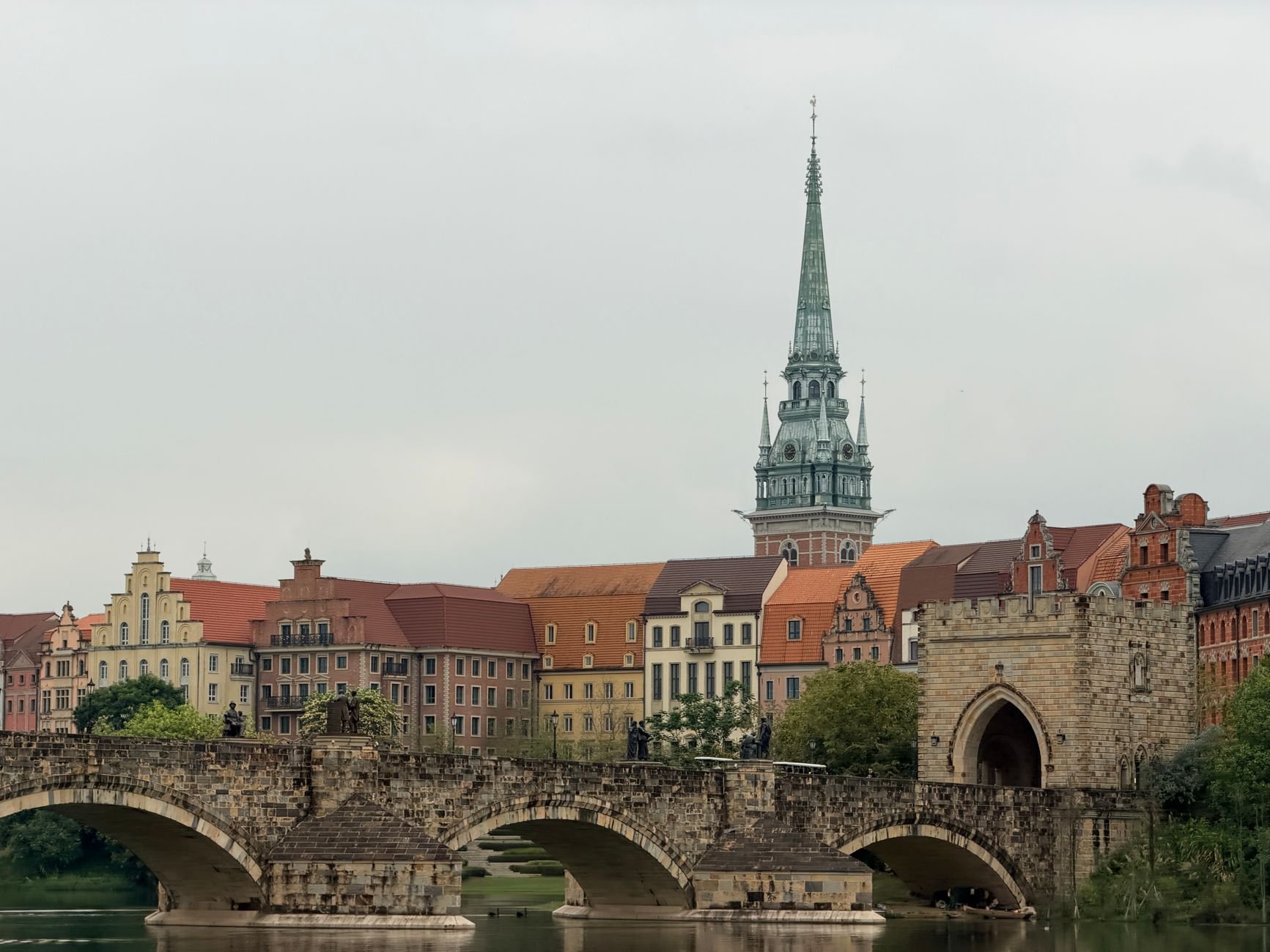 Charming European cityscape featuring a historic stone bridge and colourful old town architecture with a tall spire.